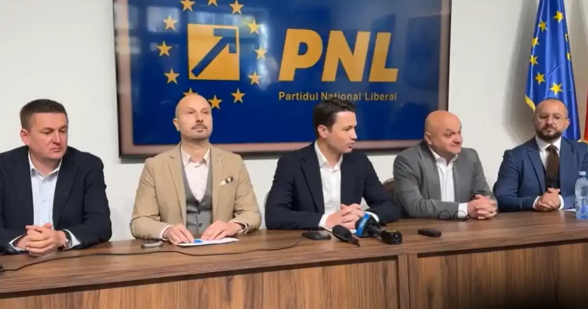 Cinci bărbați în costume așezați la o masă cu microfoane, în fața unei sigle PNL și a unui drapel al UE, la o conferință de presă.