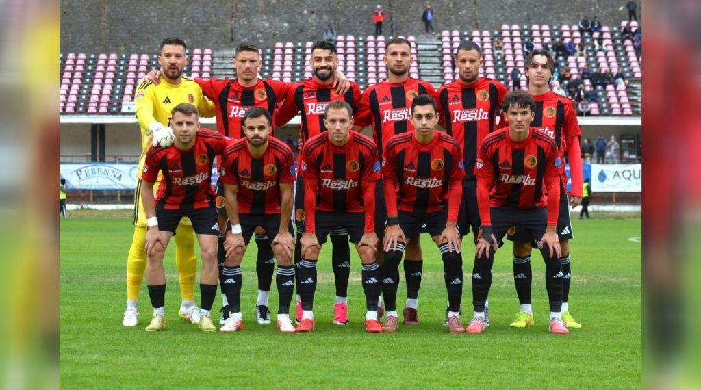 Echipa de fotbal în echipament roșu-negru cu sigla „Reșița” pe piept, la poza de grup dinaintea unui meci, pe un stadion.