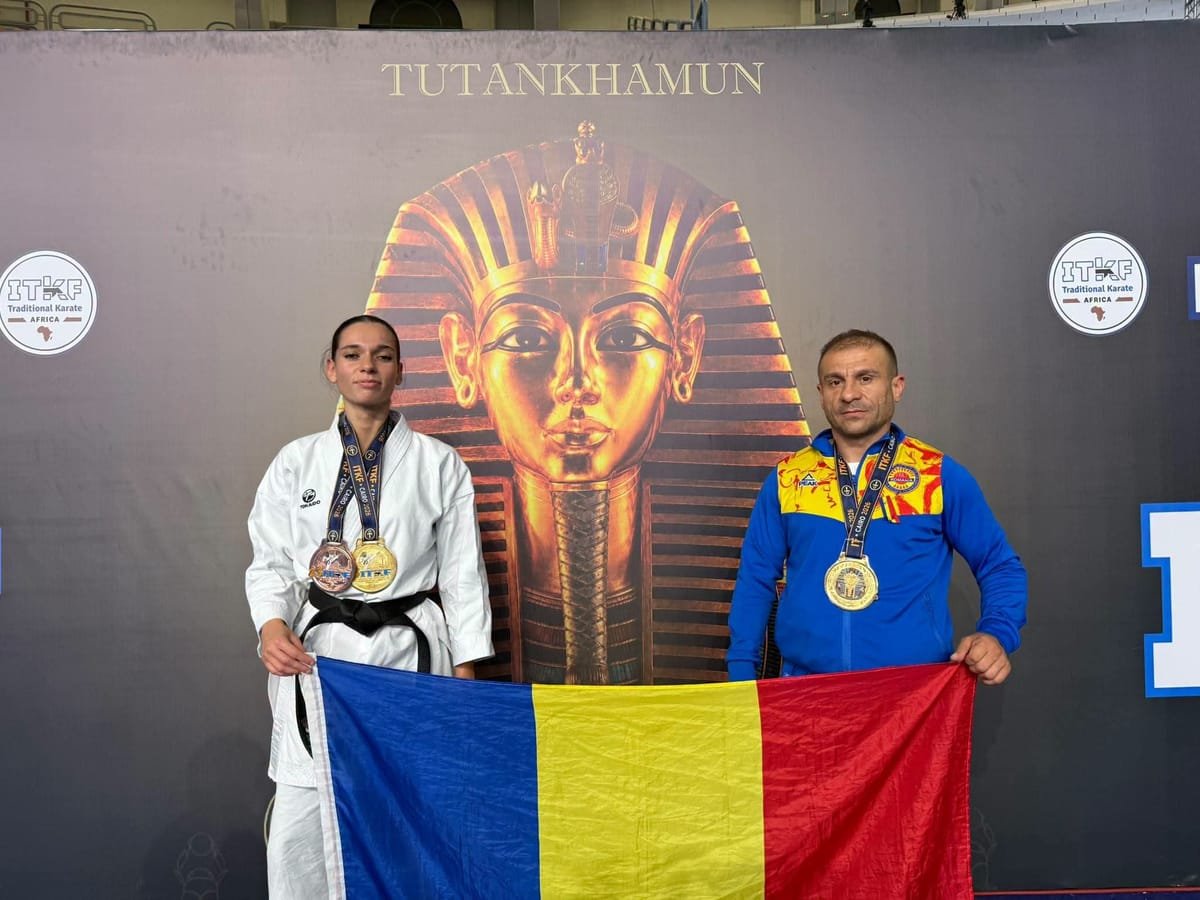 Doi sportivi români de karate cu medalii la gât țin drapelul României în fața unui panou ITF Traditional Karate Africa, Cairo, cu Tutankhamun.