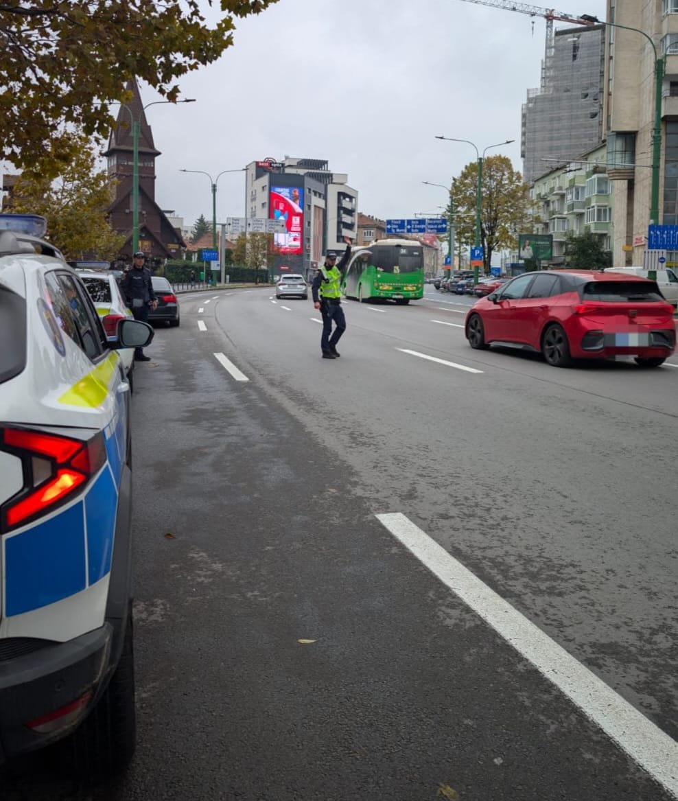 Polițiști în vestă reflectorizantă opresc și verifică traficul pe un bulevard dintr-un oraș, cu o mașină de poliție în prim-plan, un autobuz verde și o biserică